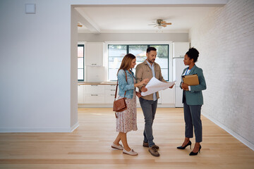 Mid adult couple analyzing blueprints with real estate agent during open house day.