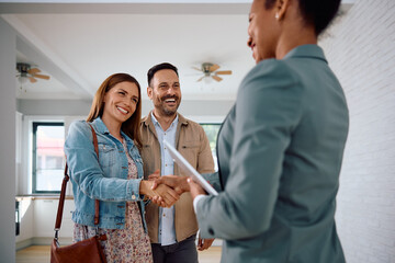 Happy woman shaking hands with real estate agent while buy new home with her husband.
