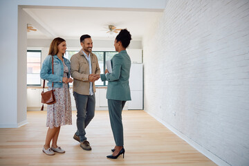 Happy couple of real estate buyers handshaking with their agent in new house.