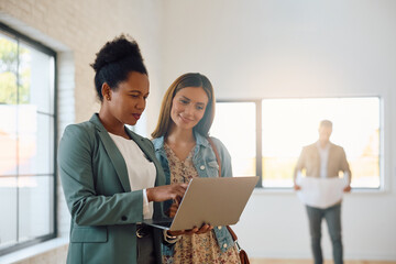 Black real estate agent using laptop while showing her buyers  new house.