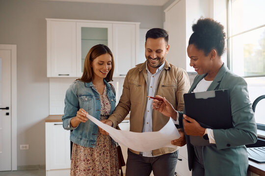 Happy man and his wife examining housing plans with their real estate agent during open house day. - Powered by Adobe