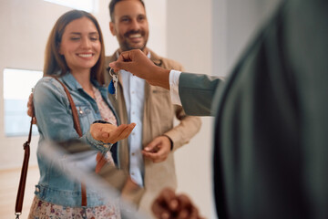Close up of happy couple receiving keys of their new home from real estate agent.