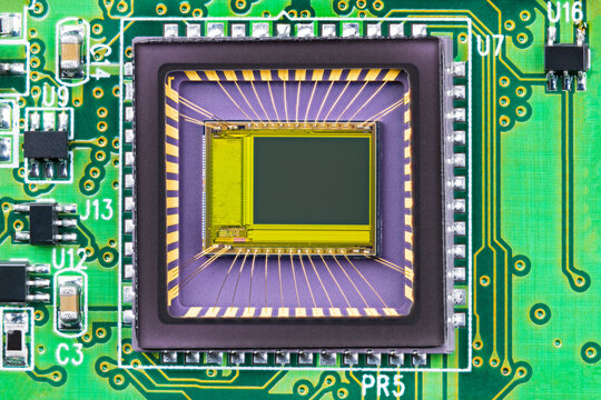 Closeup of image sensor on printed circuit board inside digital camera. Small die and gold wires in integrated chip transparent package of imager with semiconductor electronic components on green PCB.