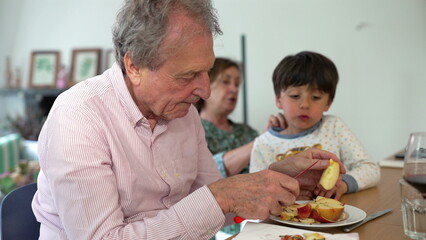 Grandfather peeling apples with his grandson at the table, while the grandmother looks on, creating a warm family bonding moment over a shared activity