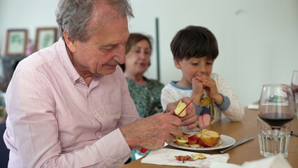 Grandfather peeling apples with his grandson at the table, while the grandmother looks on, creating a warm family bonding moment over a shared activity