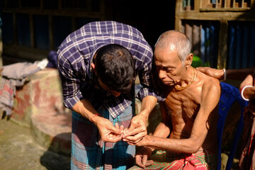 South asian rural son cutting his ill father’s nails 