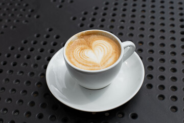 Simple serving of cappuccino coffee with heart shaped floral design.