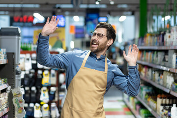 Joyful male grocery store employee wearing apron, expressing excitement and enjoyment working in...