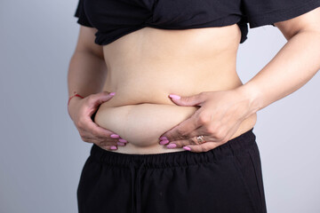 Fat woman hand holding fat belly on gray background.