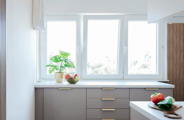 Modern interior of kitchen with beige furniture, white counter and window. Window near countertop , wooden lamers on the wall and stylish design in new apartment. Real estate.