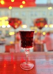 Beautiful carved crystal glass with cherry wine is on the table in a blurred bright background.