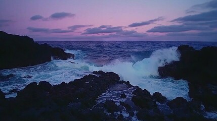 Obraz premium Large body of water adjacent to rocky shore, waves colliding with stones, and purplish sky as backdrop