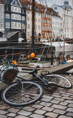 A bike dropped on the ground next to Nyhavn, Copenhagen. The waterfront, buildings and boats of the harbour are in the background.