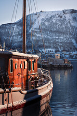 A sailing boat in the harbour of Tromsø, Norway, during winter. Snowy mountains are in the background. 