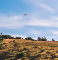 A paraglider above a hill in the Bavarian Alps, southern Germany. The skies are clear and blue.