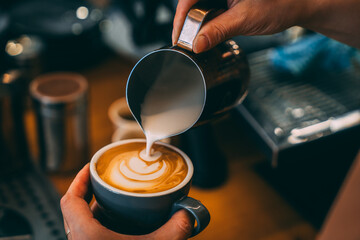 A barista pouring steamed milk into a coffee, creating some swirls of latte art. 