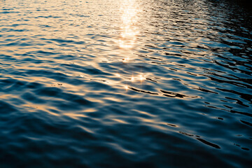 Calm ripple on water surface in evening sunshine. River, lake, pond, sea pure blue water with bright sun glares.
