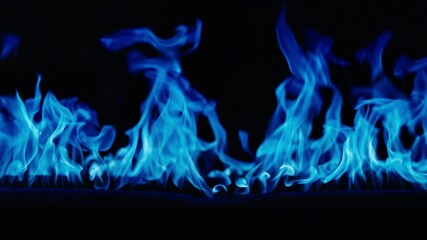 Gas burns with a bright blue flame. Blue fire is burning. Slow-motion video of bright blue flames against a black background. A wall of real fire with an abstract background. Super-slow motion video