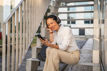 Fototapeta premium Mature japanese woman listen music on mobile phone and sit on stairs