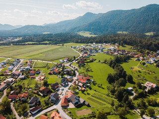 Aerial view of a picturesque village surrounded by lush green fields and mountains. The landscape features a mix of residential homes, winding roads, and agricultural land, showcasing the beauty of ru - Powered by Adobe