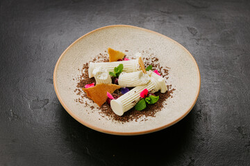 Gourmet dessert with white chocolate, biscuit shards, mint, and edible flowers on a textured plate