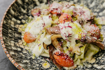 Pasta with mushrooms, cherry tomatoes, and creamy sauce topped with microgreens and Parmesan cheese
