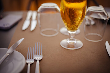 Blond golden beer served in a drinking glass on a served silverware table on brown palette, close...