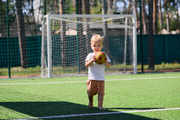 Obraz premium 2 year old boy playing with a ball on a football field