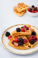 Belgian waffles decorated with strawberries, raspberries, blackberries on a light background.