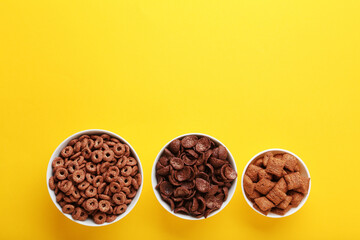 Various chocolate corn flakes in bowls on yellow background