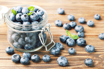 Tasty blueberries with green leafs in glass jar on wooden background