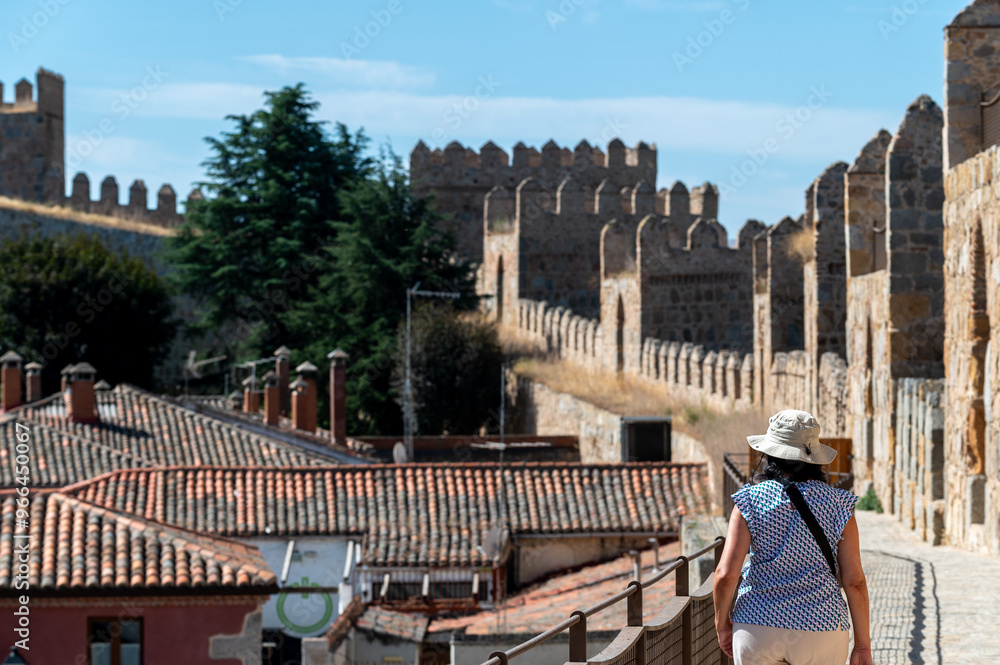 Wall mural woman with hat walking on the wall surrounding the old town of the spanish city of avila (spain) on 