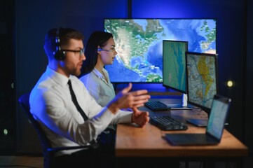 Center of dispatching maintenance. Portrait of cheerful woman and man working via headset microphone while sitting on navigation controller board