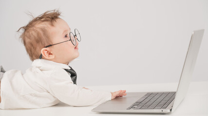Cute baby in glasses and suit working on laptop. 