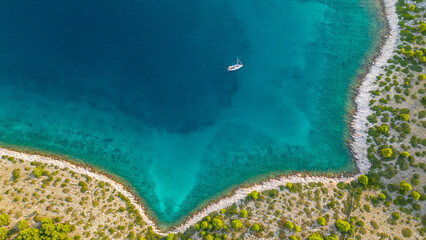 An aerial view of a serene bay on Otok Žut, located near the Kornati Islands in Croatia. The bay, surrounded by lush greenery and rocky shores, offers a tranquil retreat in the Adriatic Sea
