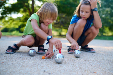Two children measure the distance between petanque balls and the target ball during a game. A...