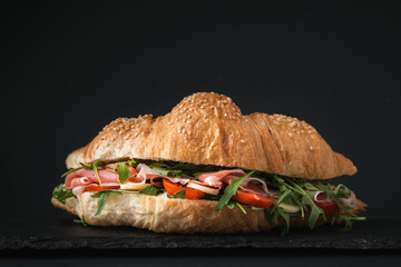 Freshly baked croissant with iberian ham, tomatoes and salad filling isolated on black background. Mock up of croissant with copy space for a free text