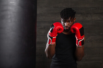 strong african american boxer in red gloves hits punching bag, muscular athlete trains punch in...