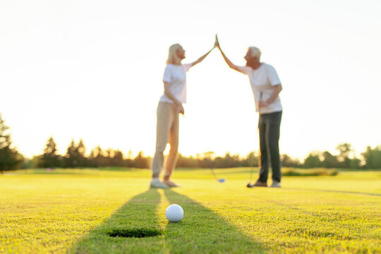 elderly senior couple in uniform celebrating victory and success in golf game and giving high five, old man and woman playing golf on golf course at sunset and doing outdoor sports
