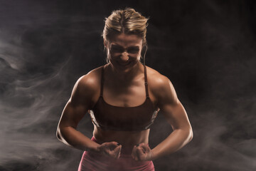 Obraz premium Strong woman flexing muscles in dramatic smoky gym setting showcasing strength and determination
