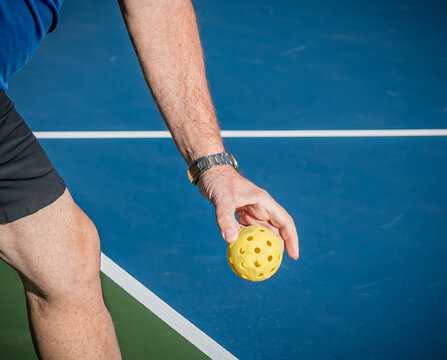 Male pickleball player holds the ball low in preparation to hit a serve