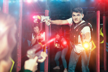 Naklejka premium Portrait of positive young man with laser gun having fun with her friends on lasertag arena