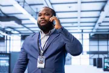 Supervisor discussing on mobile phone in high tech data center housing advanced computing hardware. Professional delegating tasks in futuristic server farm during telephone call