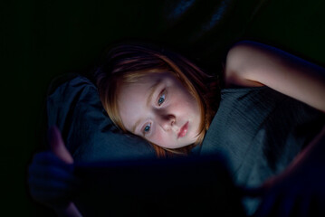 low-light portrait of a girl using a screen at night, with the. blue light reflecting on her face.