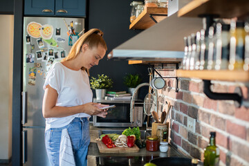 Smiling young woman using smartphone in modern kitchen