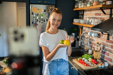 Smiling young woman cooking and filming with smartphone in modern kitchen