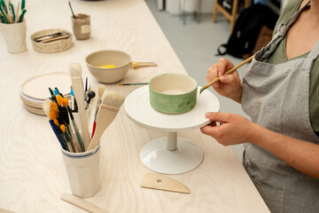 Girl is decorating a clay product with bright green color. Using a brush to paint a ceramics bowl. Learning how to paint a handmade pottery project.