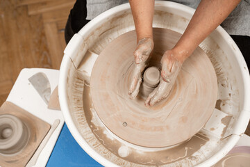 Fototapeta premium Girl is making a bowl on a pottery wheel with your own hands. Forming the proper size and shape of pottery with increasing speed of a pottery wheel.