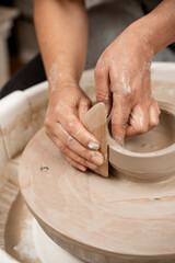 Girl is making smooth edges of pottery with a wooden scraper and a pottery wheel. Cutting the lines...