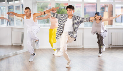 Active young guy practicing hip-hop reject step in training hall during dancing classes